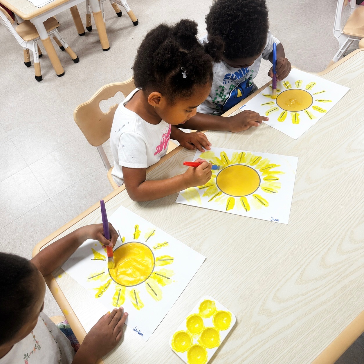 Children painting bright yellow sun artwork together at a classroom table
